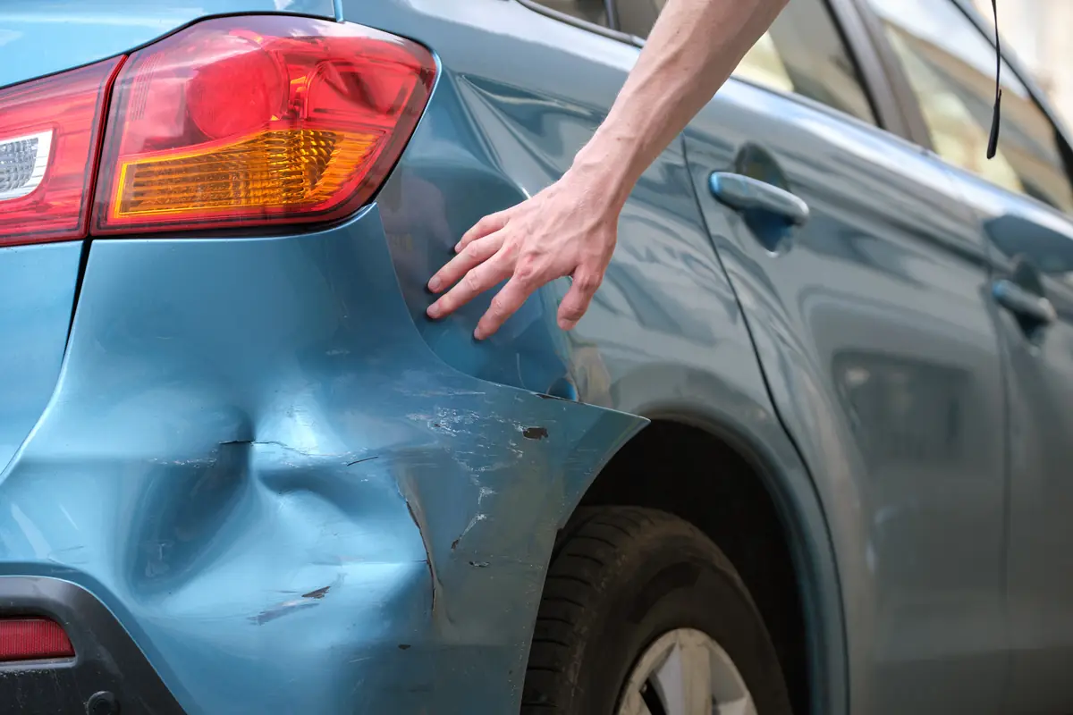 Junk car offer drop at pickup: hand on a dented car door Hand on a dented car door, the kind of damage cited in a junk car offer drop at pickup