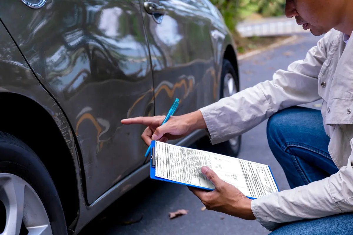 Insurance adjuster writing notes beside a damaged car, part of a car insurance flood damage claim