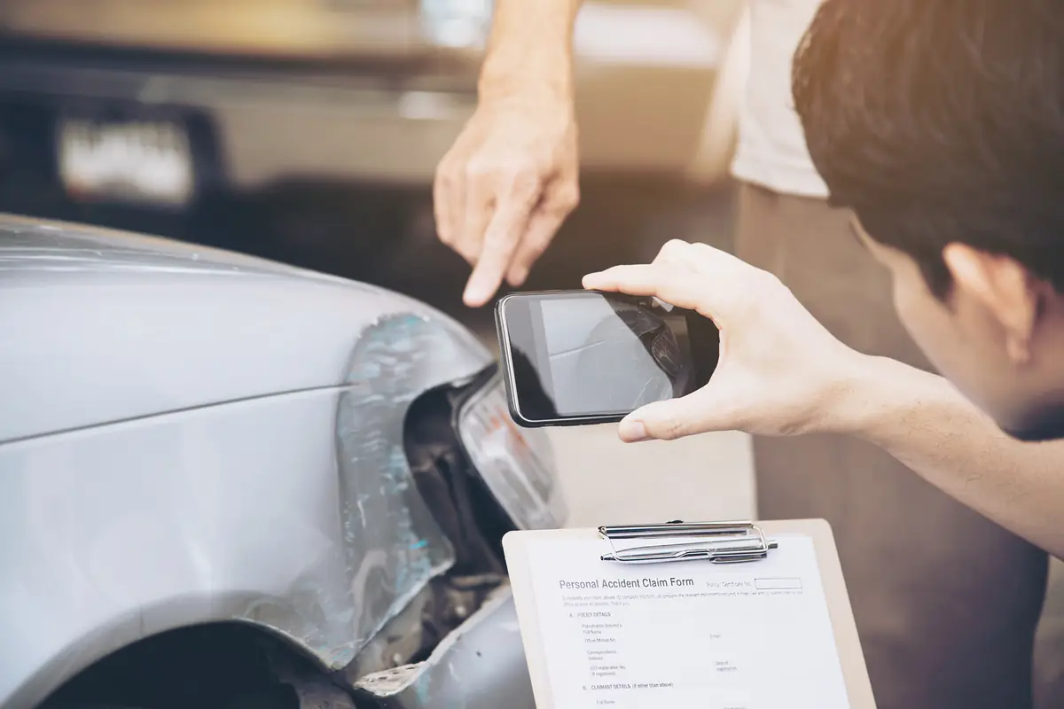 Adjuster photographing car damage with a claim form, the insurance step when a teen totaled their first car in Texas