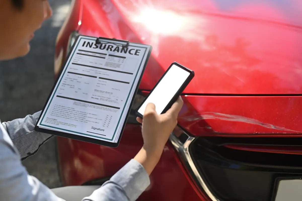 Hail damage claim denied in Texas: adjuster holding an insurance claim form beside a car Adjuster holding an insurance claim form beside a car, reviewing a hail damage claim denied in Texas