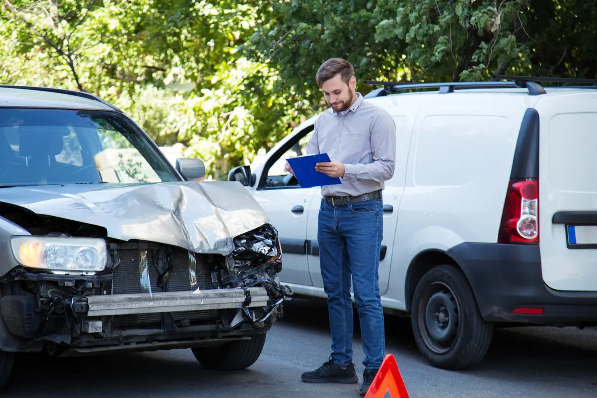 Insurance agent with a claim form beside a crashed car, preparing a total loss offer in Texas