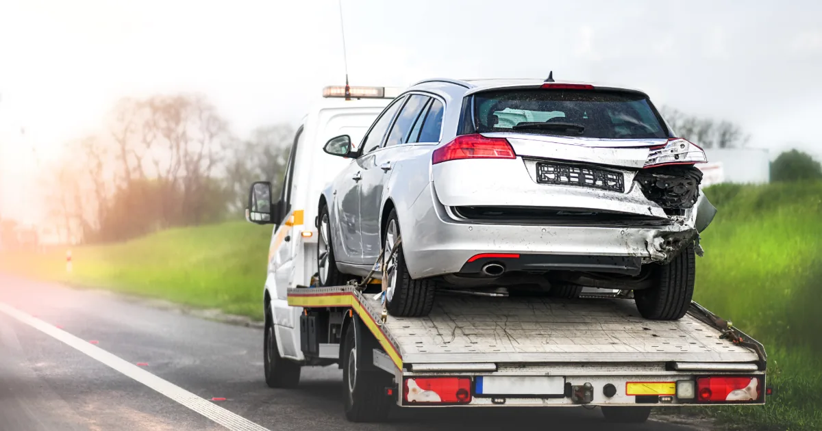 Silver station wagon with rear-end damage loaded on a flatbed tow truck at a Texas roadside — junk car buyer lowered the offer at pickup