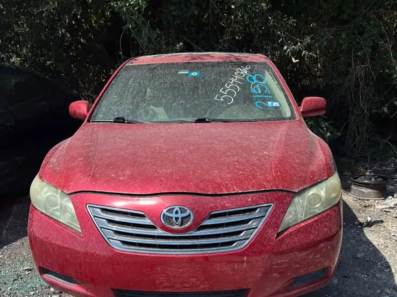 Red 2009 Toyota Camry Hybrid SE junk car bought for $1,200 in Amarillo, TX. Weathered paint, sitting on a lot.