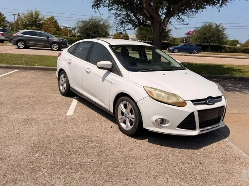 White 2013 Ford Focus junk car bought for $1,200 in Houston, TX. Faded headlights, worn paint.